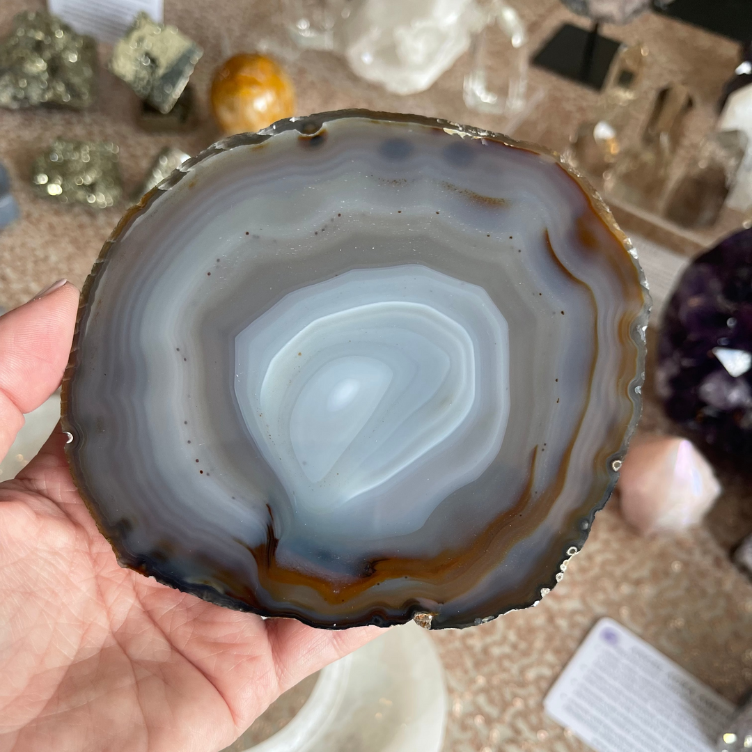 Agate slice held in a hand with a display of crystals in the background