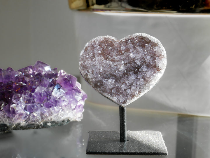 Heart-shaped crystal on a stand next to a purple amethyst crystal